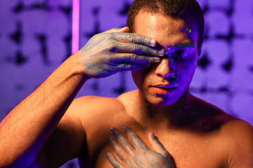 Young African-American man with fluorescent paint on his skin on color background