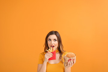 Portrait of beautiful young woman with burger and french fries on color background