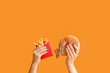 Female hands with french fries and burger on color background