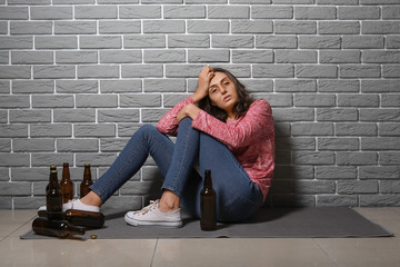 Young drunk woman near brick wall. Concept of alcoholism