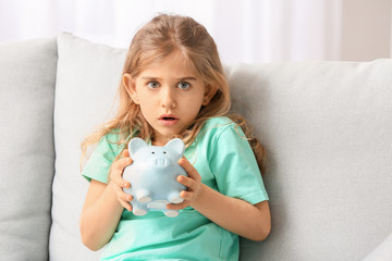 Scared cute girl with empty piggy bank at home