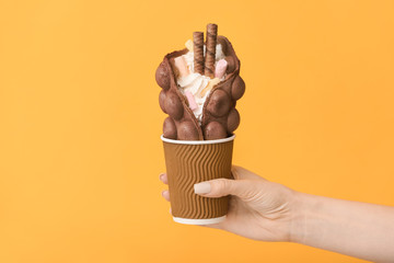 Female hand with delicious sweet bubble waffle on color background
