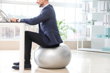 Businessman sitting on fitness ball while working in office © Pixel-Shot