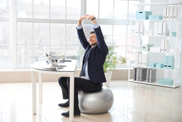 Businessman sitting on fitness ball while working in office
