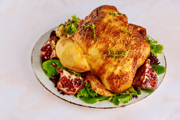 Grilled whole chicken on plate with green salad and pomegranate.