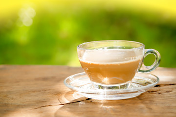 milk coffee in a coffee cup on a vintage old dark wooden table texture and blurred green leaf background