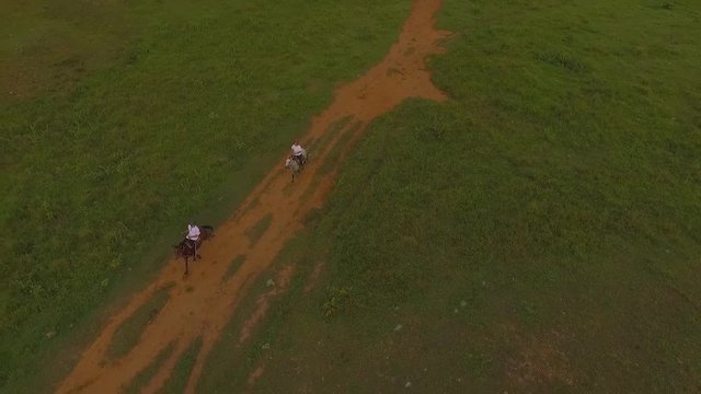 Slow motion aerial view of two riders galloping their horses in a venezuelan plain