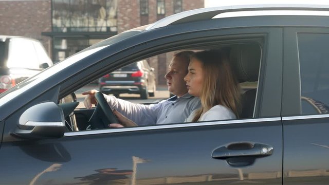 4k video of male driving instructor sitting on passenger seat in car and showing way to female student in driving school