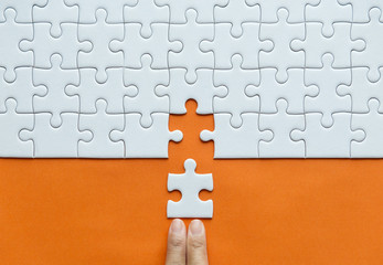 Hand putting jigsaw puzzle white color on orange background