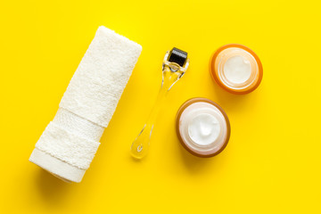 Cosmetology and skin care concept. Cream near dermaroller on yellow background top-down