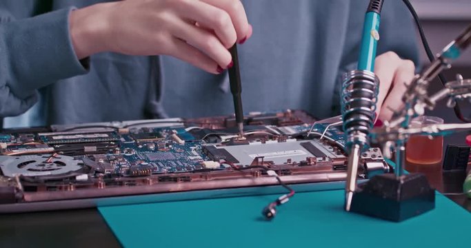 Woman electronics engineer is soldering an electric board in her workshop. Girl student are studying electronics and soldering in classroom.
