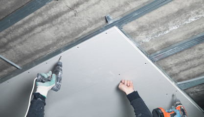 Worker with a drill screwdriver twists the screw into the drywall.