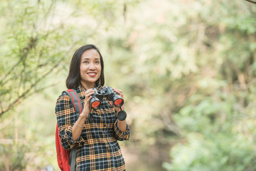 Fototapeta premium hiking women use binoculars to travel and have a happy smile. tourist looking through binoculars considers wild birds in the jungle. bird watching tours. with backpack. travel concept