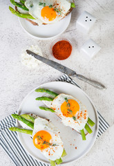 Crispy toast with cream cheese cream, fried egg and asparagus in a plate on a white background.