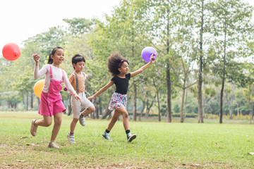 Fototapeta premium happy children playing with colorful toy balloons outdoors. Kid having fun in green spring field against blue sky background. happy multi-ethnic children playing. freedom and imagination concept.