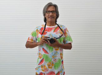 Smiling happy elderly traveler asian man wearing summer shirt and eyeglasses holding film camera in...