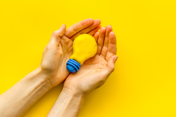 Idea concept. Bulb in hands on yellow background top-down copy space