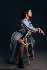 The girl is sitting on a white chair in a masculine pose.