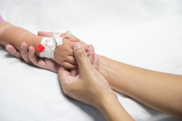 Mother holding baby hand give saline solution in bed fever patients in hospital.