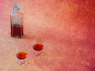 Crystal bottle of cognac and two glasses with a drink on a brown abstract background.