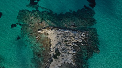 Aerial view of Vourvourou beach, small peninsula in turquoise water of Aegean sea. Waves beating cliff rocky coastline. Halkidiki, Greece.