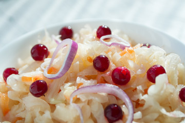 Sauerkraut with cranberries and onions in a white cup, closeup. The concept of proper nutrition and healthy eating. Selective focus, copy space for text.