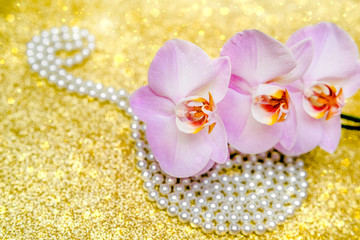 purple Orchid and pearl necklace on a shiny gold background.