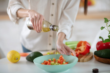 Hands of a young woman pouring olive oil into a salad.