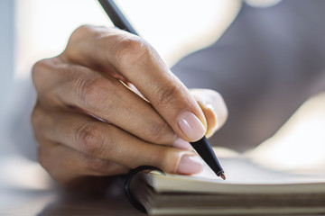 Woman writes with a pen in notebook in a sunny office, business and education concept. Close up