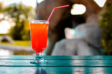 Fresh exotic red cocktail with ice cubes and orange on a wooden table