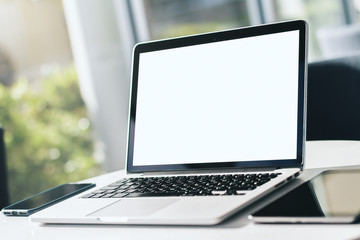 Fototapeta premium Close up of modern laptop with blank screen on white table in sunny interior, mockup. Business and technology concept