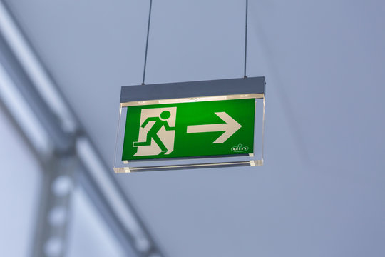 Vienna, Austria - Jan 29, 2020: View on illuminated emergency exit sign. With running figure and arrow to the right. Neutral, white background. Modern design. Hanging from the ceiling.