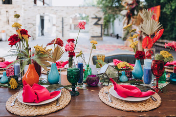 Banquet tables decorated in tropical style decor, dishes on the tables with pink napkins, glasses, candles, colorful flowers