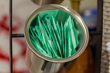 Munich, Bavaria / Germany - Feb 15, 2020: Sugar sachets in a metallic bowl. Many small, green paper...