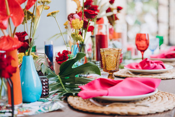 Banquet tables decorated in tropical style decor, dishes on the tables with pink napkins, glasses, candles, colorful flowers