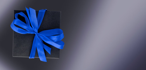 Black textured gift box with a blue bow on a gradient dark background. Top view. Copy space.