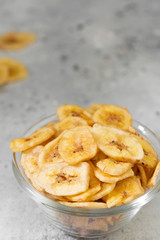 Dried bananas in a glass bowl on a gray kitchen table. Banana chips. Vegetarian snack for proper nutrition	