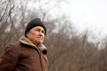 Elderly man looks into the distance on forest background. Sad face expression, concept of cold...