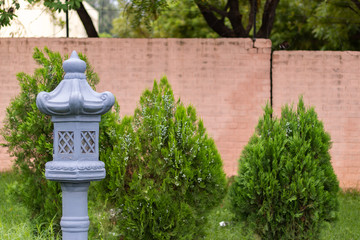 A blue medieval style lamp post for oil lamps with red brick wall and thuja plants in the background. Buddhism and spirituality concept