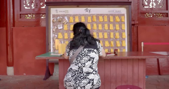 Female writing prayer on a joss paper at Confucius temple in Tainan. Taiwan. Rear view push in.