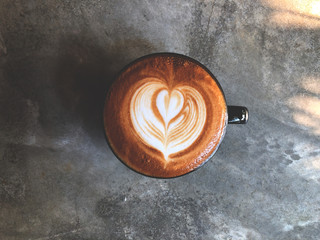 heart love shape latte art coffee in Black cup on cement background with natural dark light , vintage style and copy space. Object placed to the center.