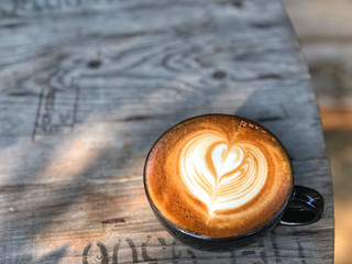 Heart shape latte art coffee in Black cup on the vintage wooden table with natural light. Love coffee love in your cup.