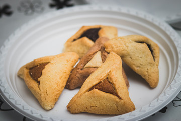 Hamantaschen. (ozen haman). Jewish food for Purim. Triangular crispy dough, stuffed with dates, halva and chocolate, on a white plate.