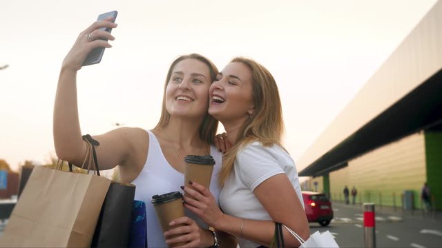 4k closeup video of two happy smiling girls making selfie on smartphone camera after doing shopping in big mall