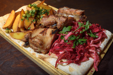 Pork ribs, rustic potato and beetroot salad on pita bread on a wooden tray. Close-up. Tasty food.