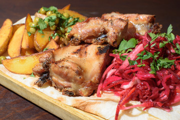 Pork ribs, rustic potato and beetroot salad on pita bread on a wooden tray. Close-up. Tasty food.