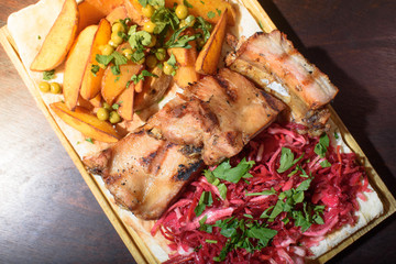 Pork ribs, rustic potato and beetroot salad on pita bread on a wooden tray. Close-up. Tasty food.