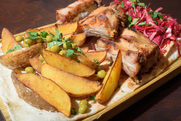 Pork ribs, rustic potato and beetroot salad on pita bread on a wooden tray. Close-up. Tasty food.