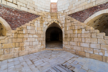 Symmetric exterior shot of ancient brick building with two shabby stone stairways leading to closed picket gate and two crumbling arched alcoves on street