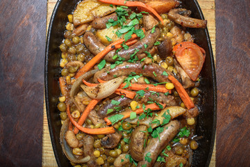 Hungarian frying pan (pork and beef sausages stewed with vegetables in dark beer) on a large wooden board. Tasty and healthy food. Close-up.